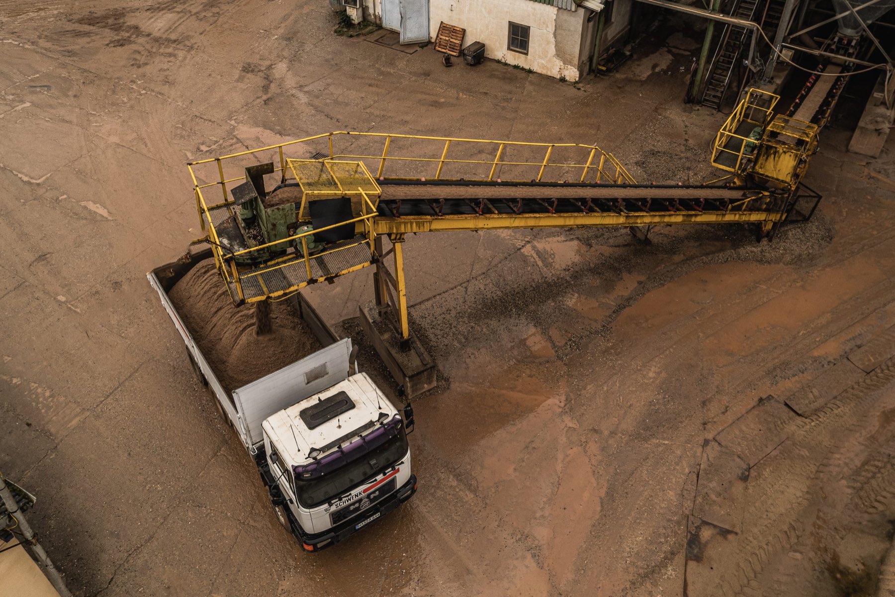 Blick von oben auf das Werk: ein Förderband lädt Schüttgut auf die Mulde eines Lkw.